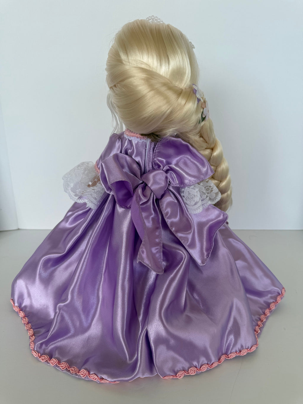 The Doll Maker 12-inch Rapunzel doll wearing a purple satin gown with lace sleeves and a large back bow