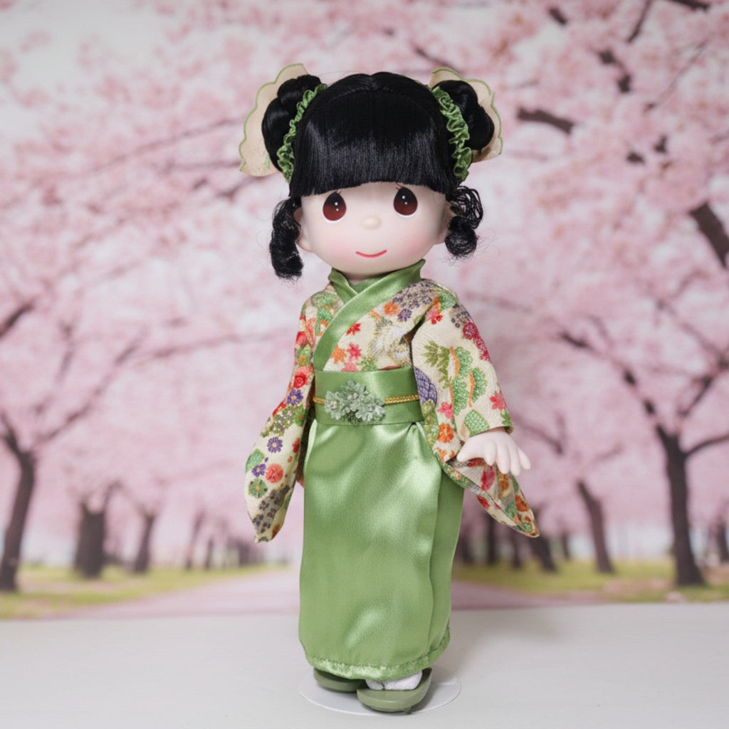 The Doll Maker Rui doll wearing a green floral kimono for Japanese Girls' Day, standing before a cherry blossom backdrop
