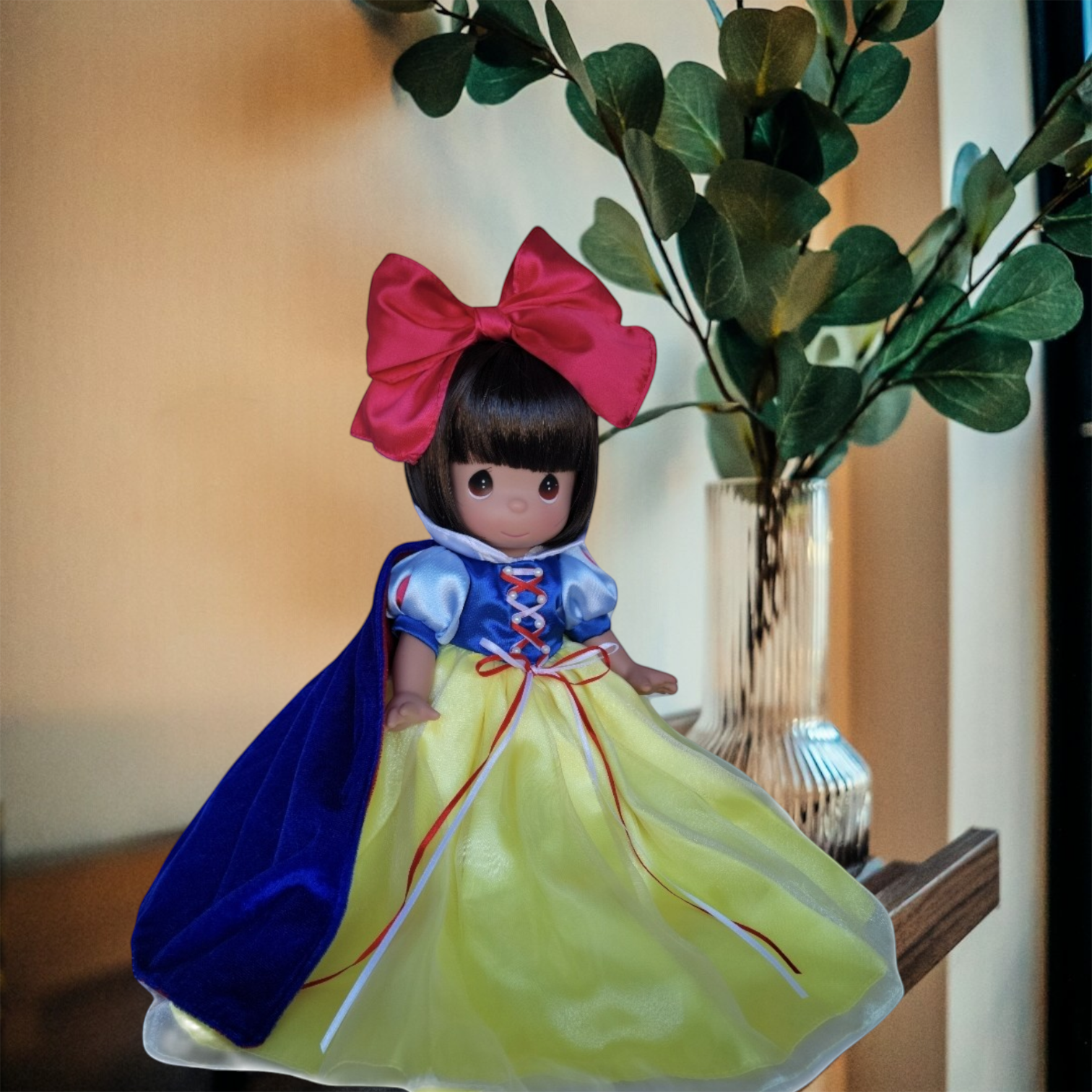 The Doll Maker 12-inch Snow White collectible doll with a red bow, blue velvet cape, and yellow satin skirt.