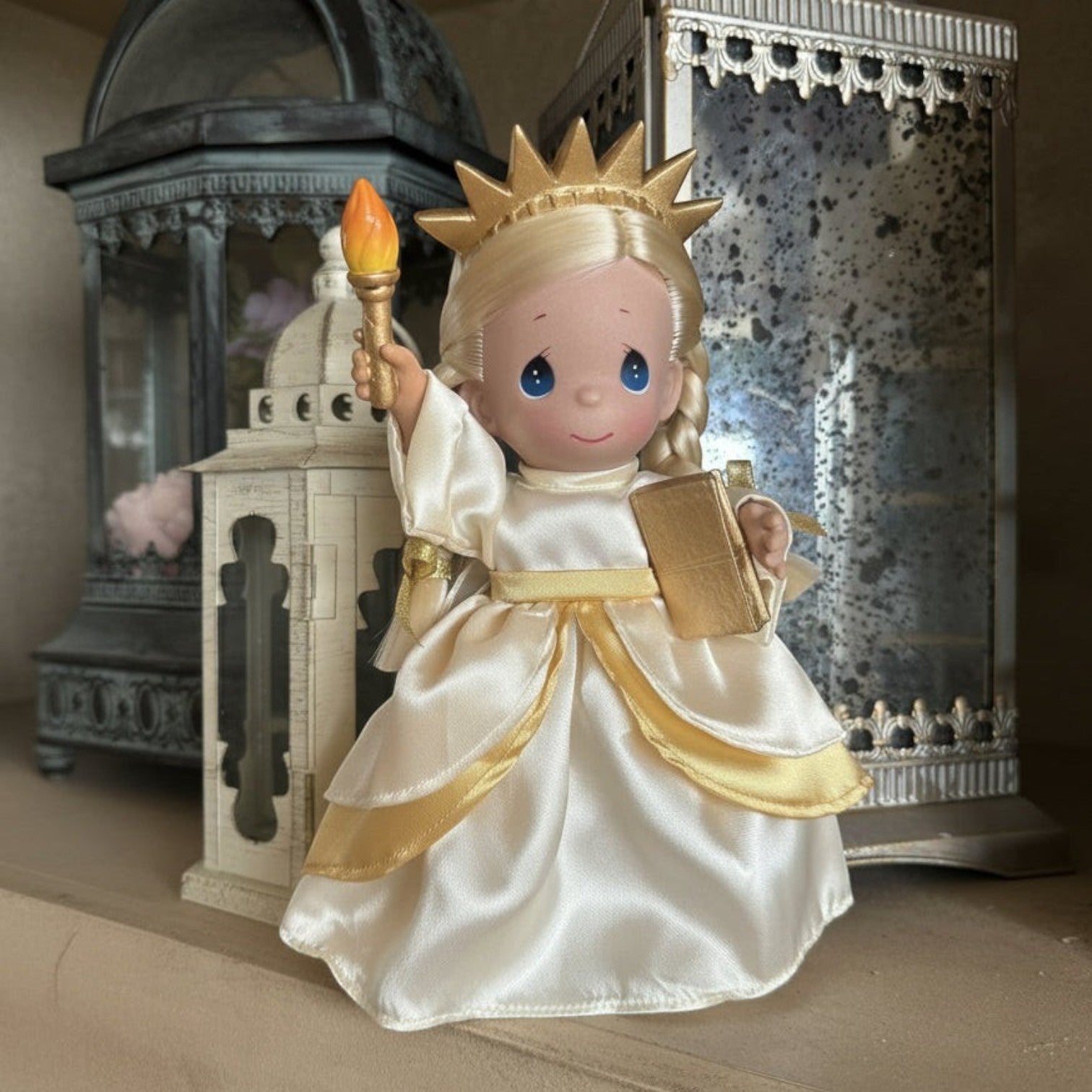 The Doll Maker 9-inch Statue of Liberty doll in an ivory and gold dress, holding a torch and book for USA anniversary.