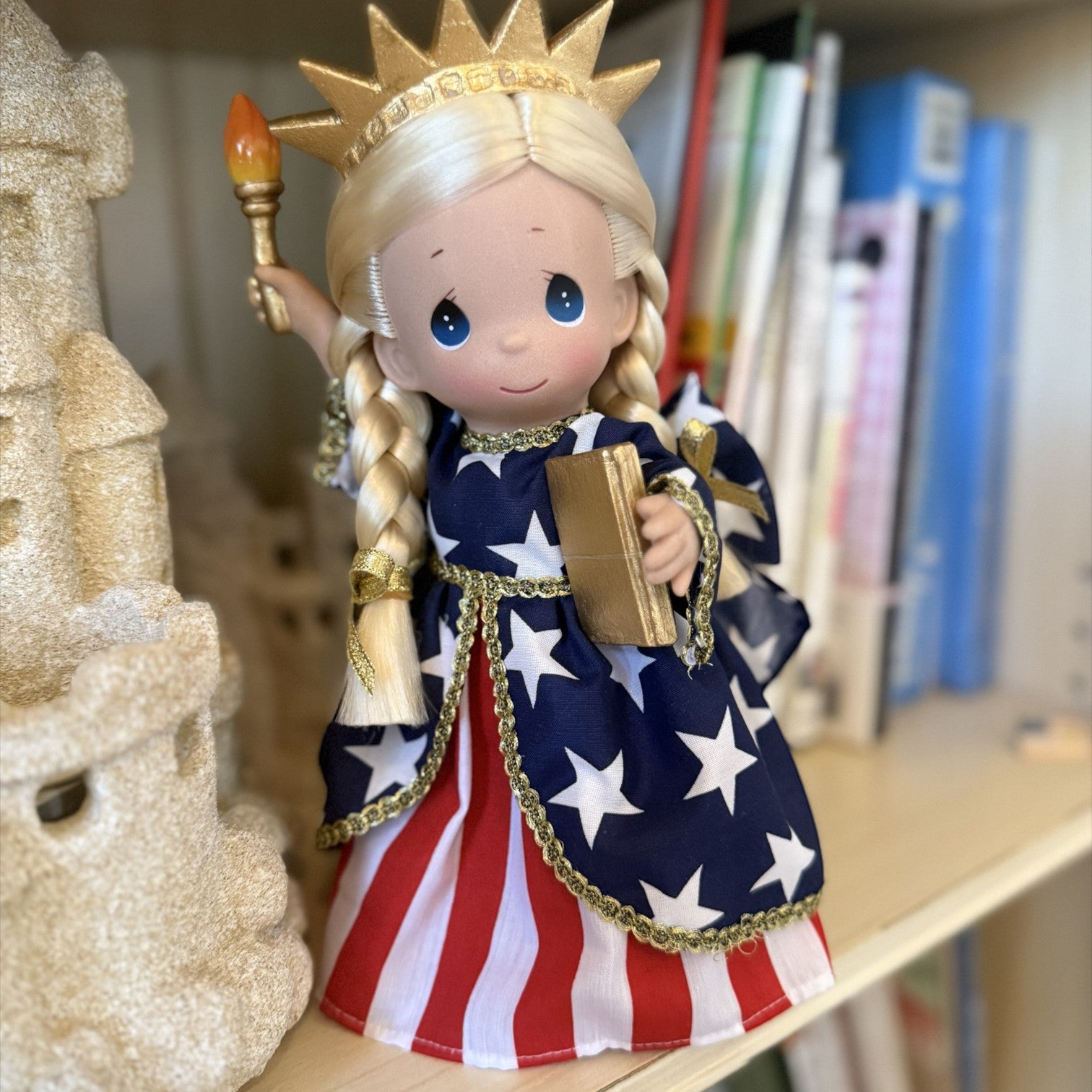 The Doll Maker 9-inch Statue of Liberty doll in a patriotic red, white, and blue star-patterned dress with gold crown.