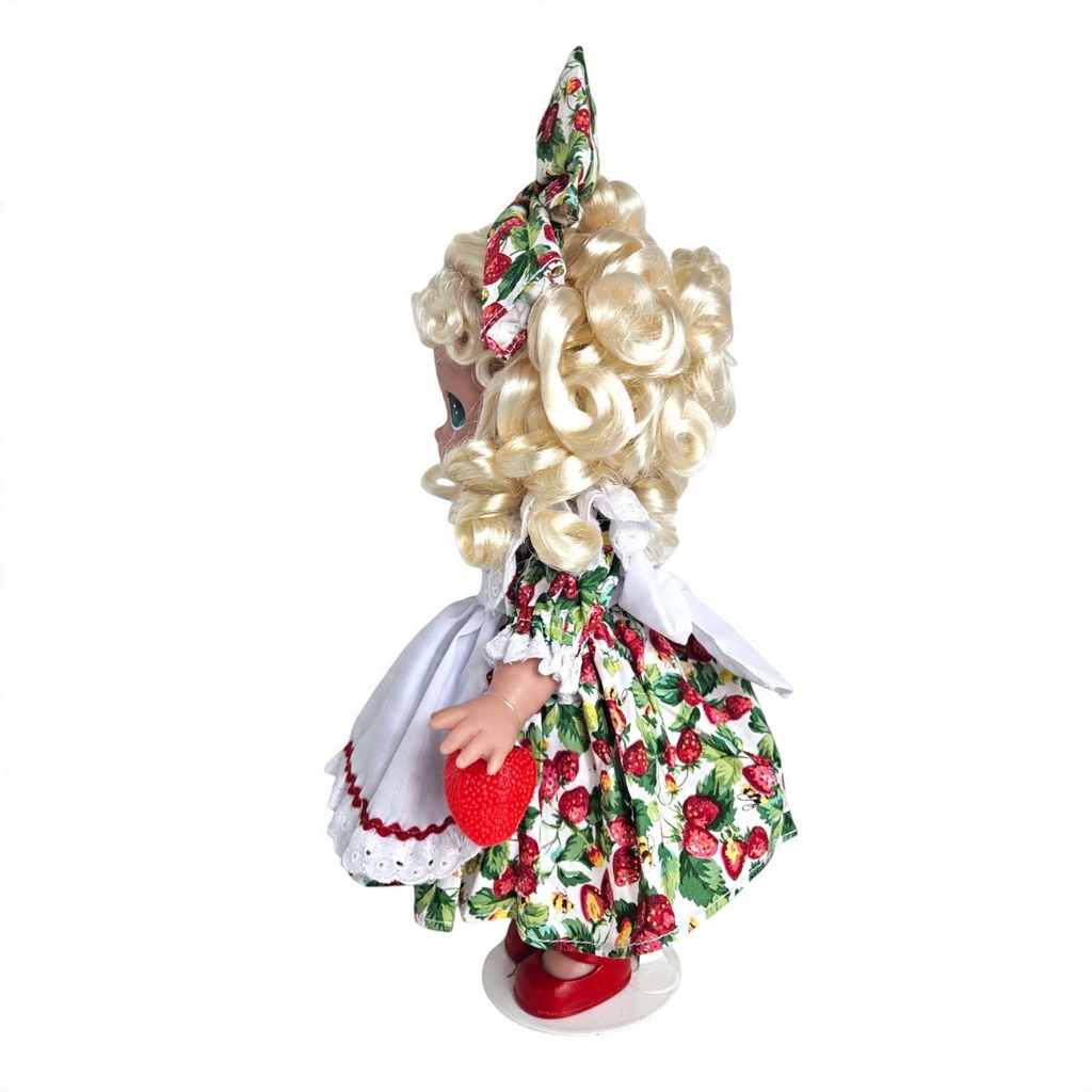 The Doll Maker You’re Berry Sweet 12-inch vinyl doll with blonde curls wearing a strawberry print dress and hair bow.