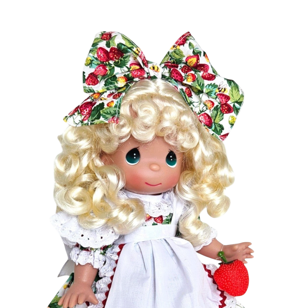 The Doll Maker You’re Berry Sweet 12-inch vinyl doll with blonde curls, strawberry print dress, and matching bow.