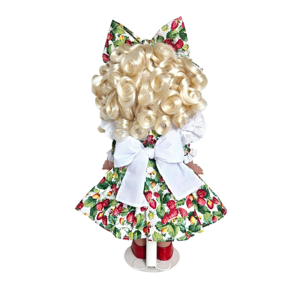 The Doll Maker You’re Berry Sweet 12-inch vinyl doll with blonde curls, strawberry print dress, and large back bow.