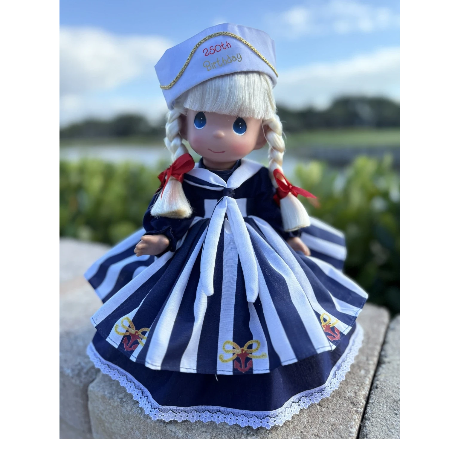 The Doll Maker 12-inch commemorative USA 250th birthday doll in a navy and white sailor dress with anchor print.