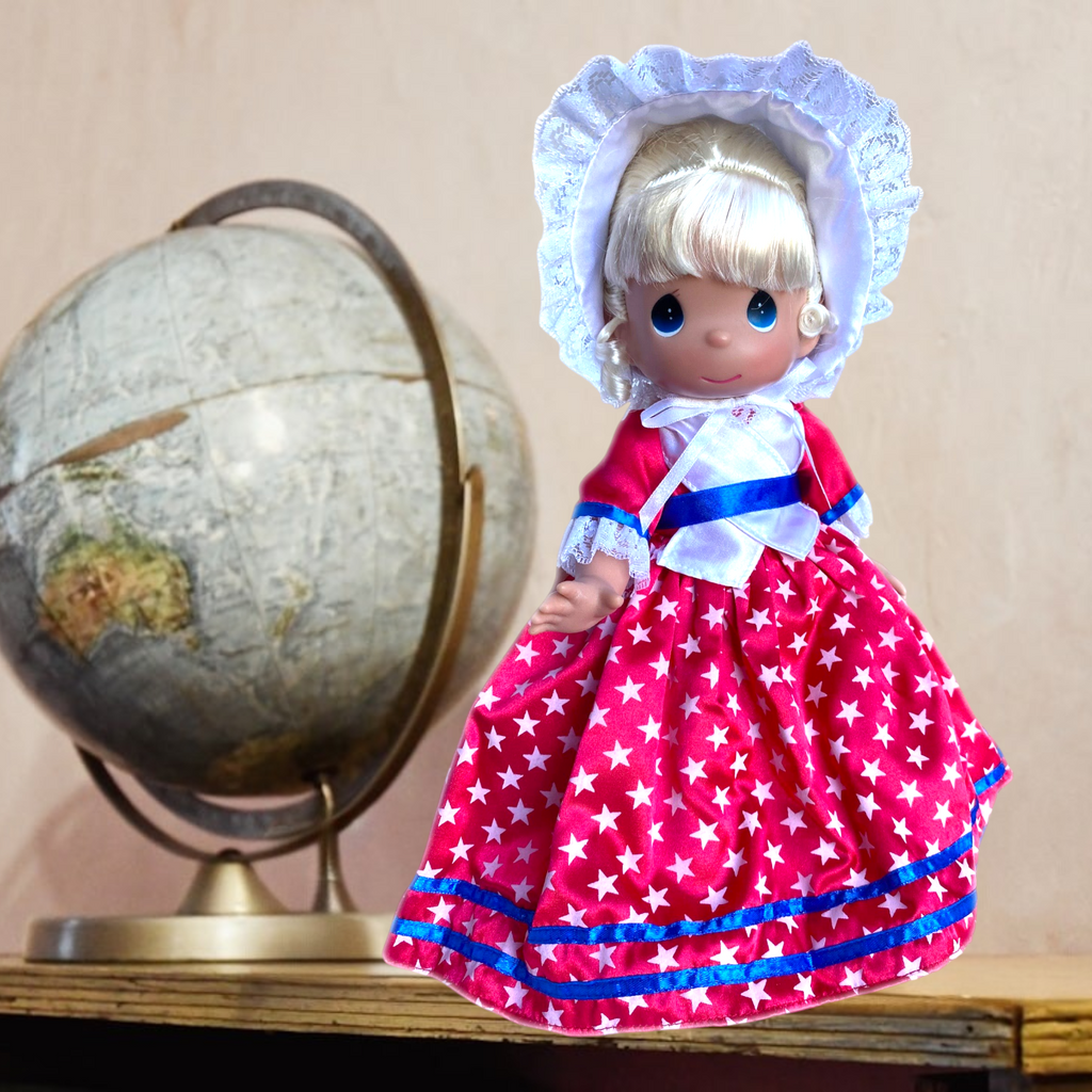 The Doll Maker 12-inch USA collectible doll wearing a red star-print dress with a white bonnet and globe background