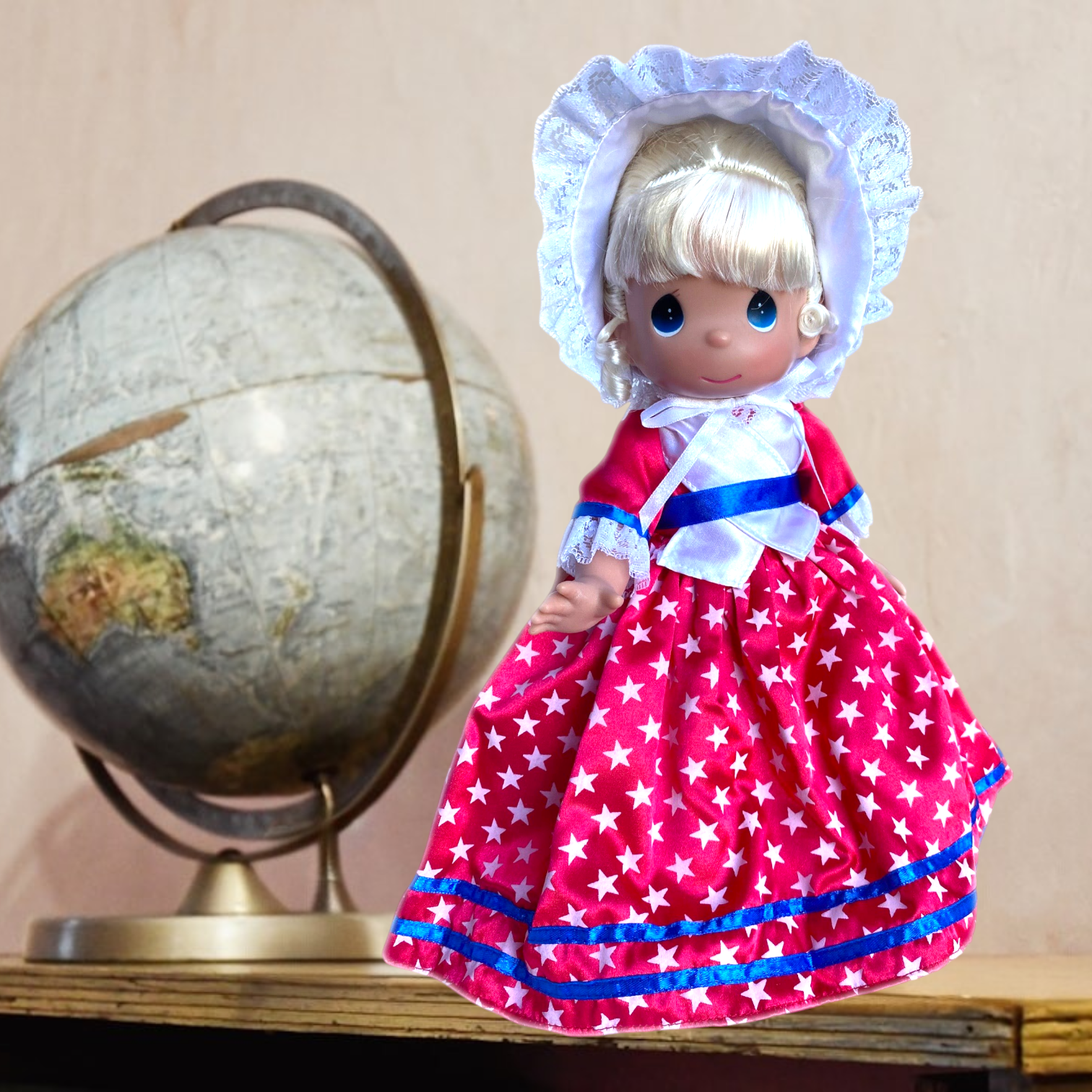 The Doll Maker 12-inch USA collectible doll wearing a red star-print dress with a white bonnet and globe background