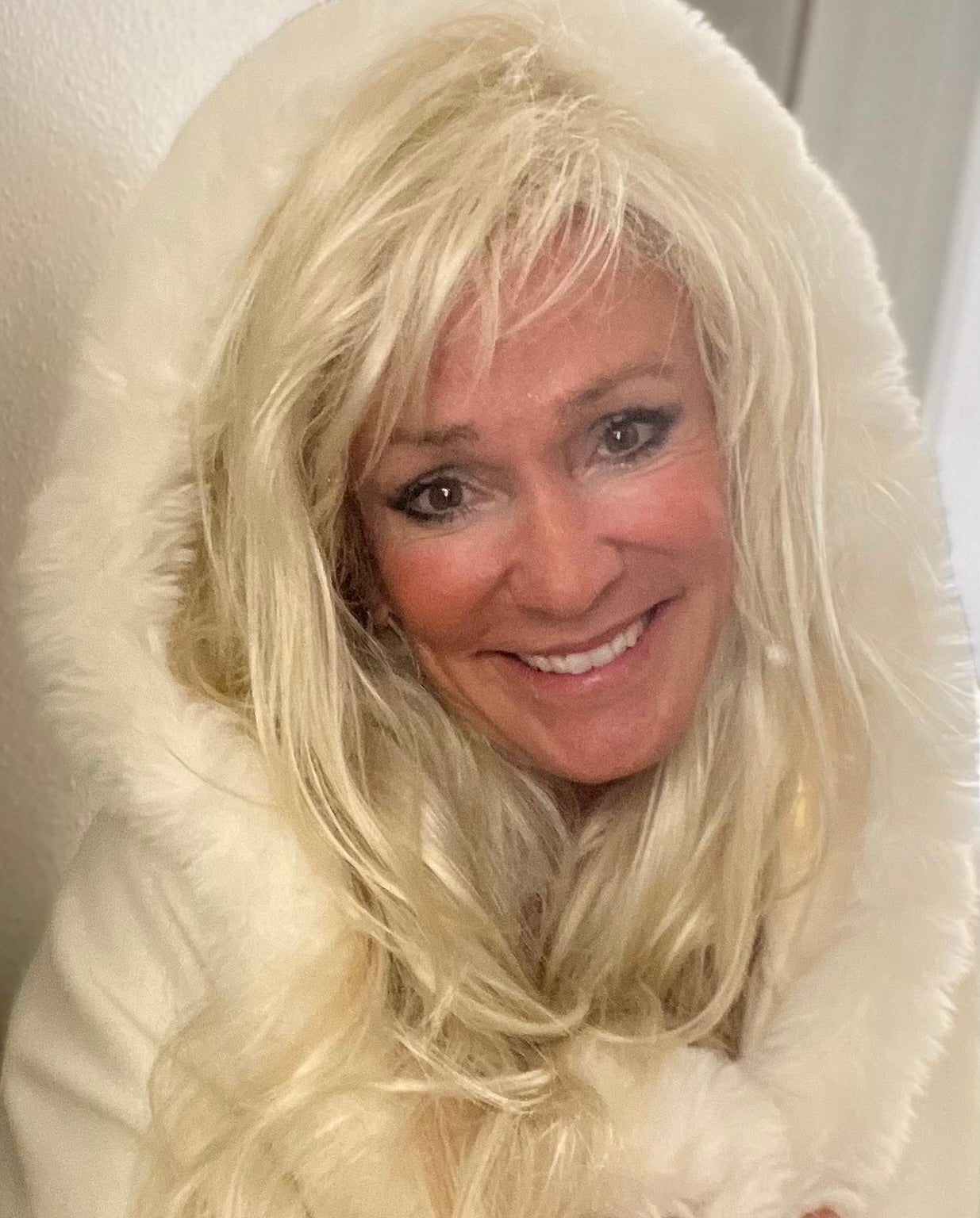 White hooded winter cape with plush fur trim worn by Linda Rick for a cozy holiday look