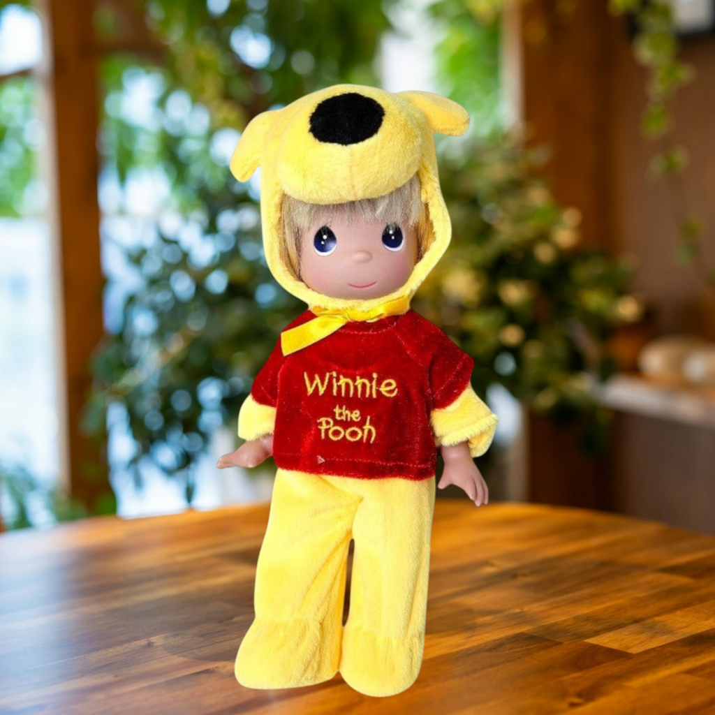 The Doll Maker 12-inch Winnie the Pooh collectible doll wearing a plush yellow bear hood and red embroidered shirt.