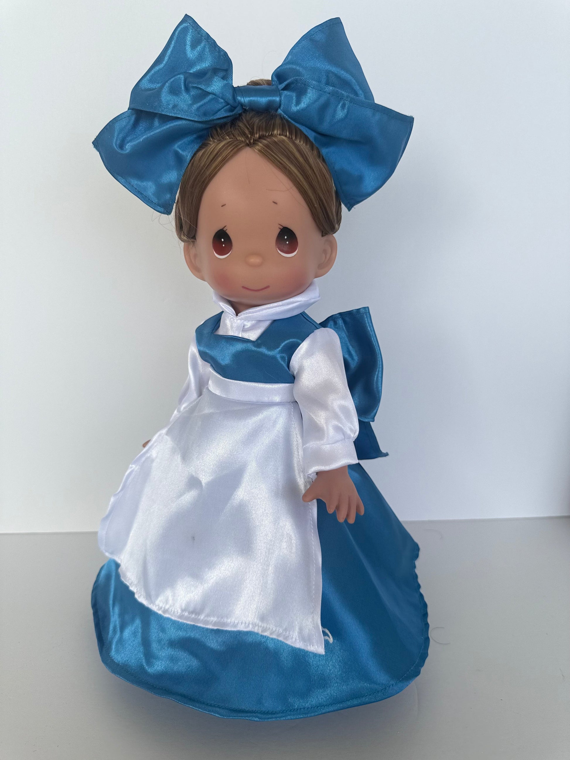 The Doll Maker's 12” Belle doll in a blue satin dress with white apron and large blue bow.