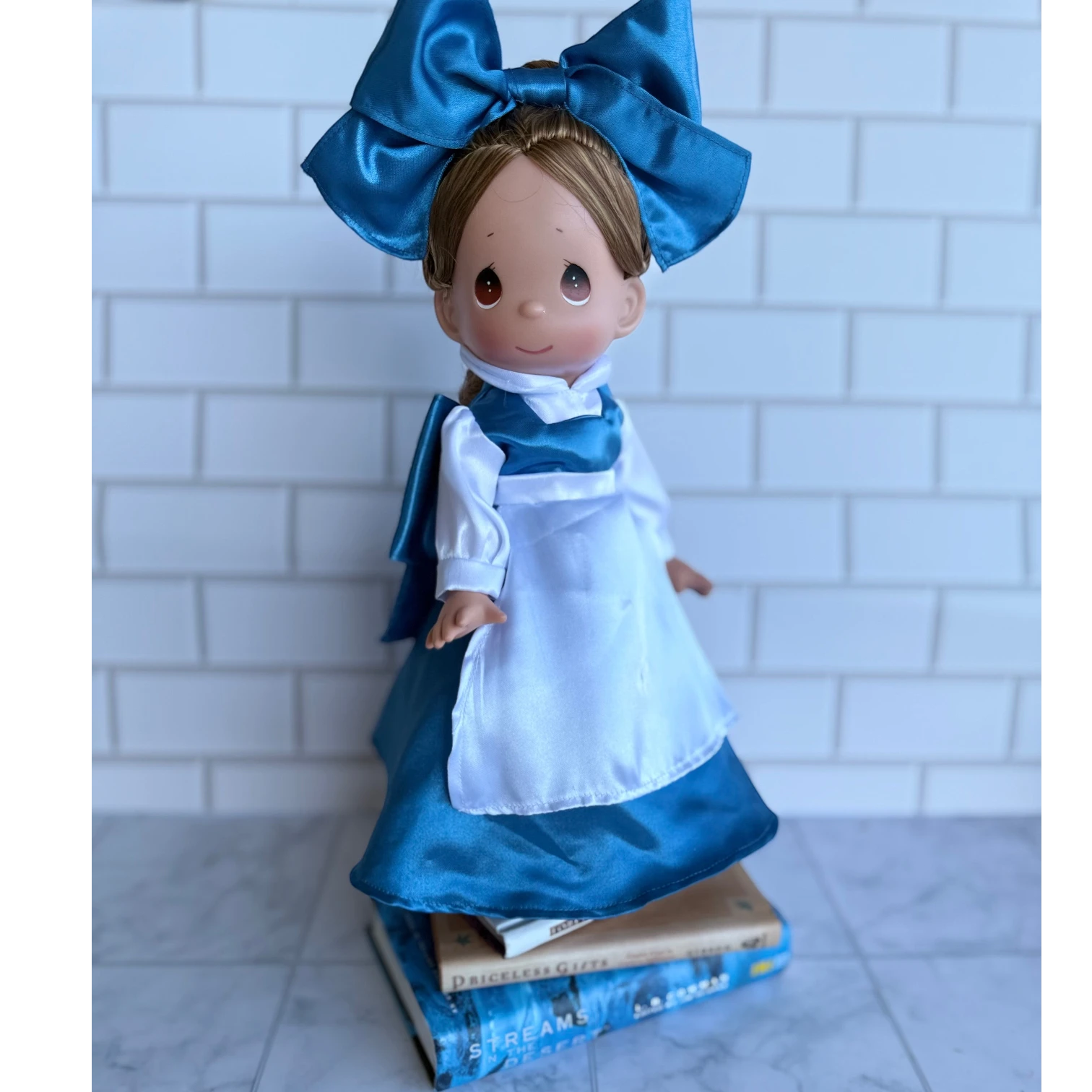 The Doll Maker's 12" Belle doll in a blue satin dress with white apron and large blue bow.