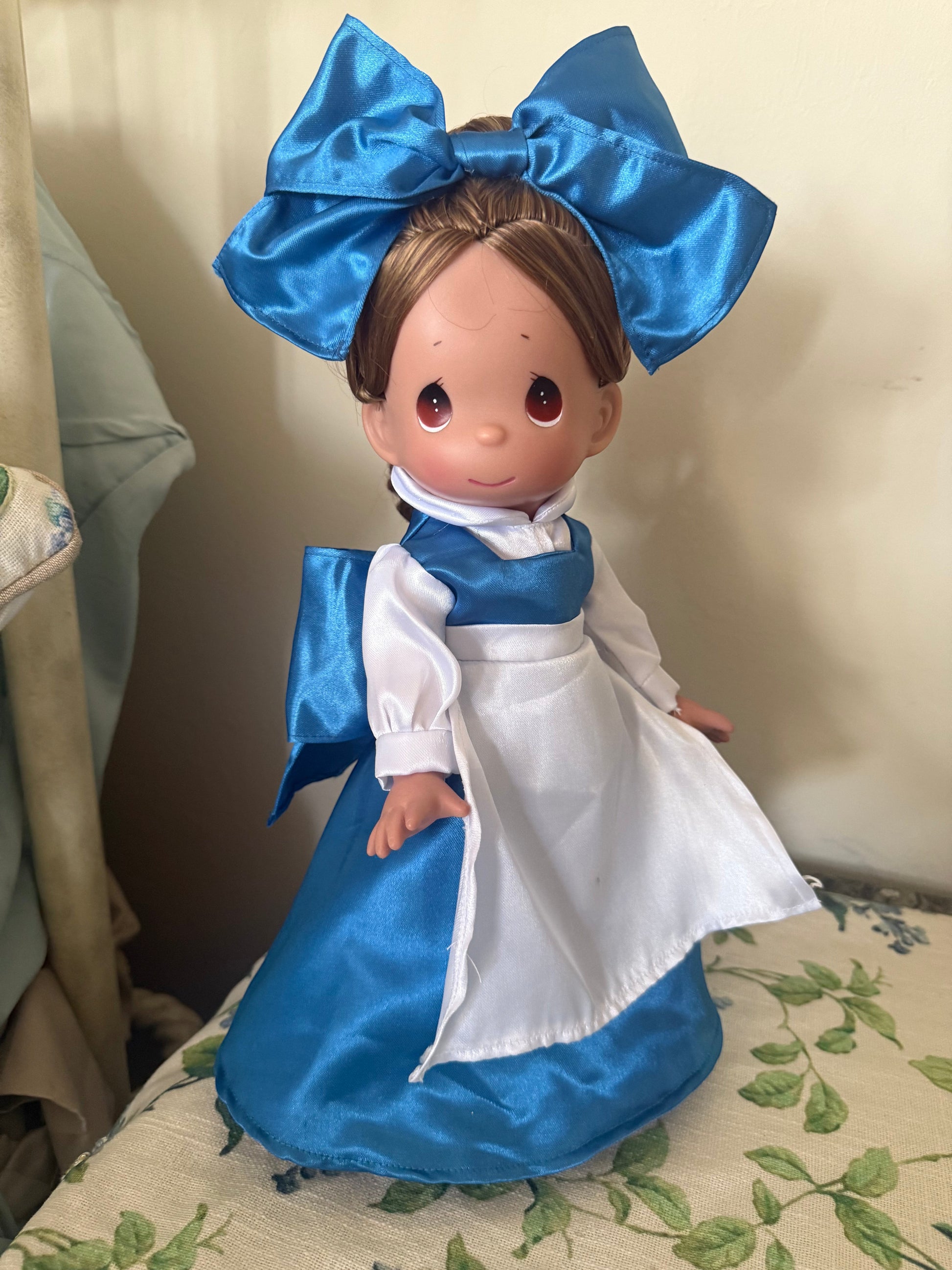 The Doll Maker's 12" Belle doll in a blue satin dress with white apron and large blue bow.