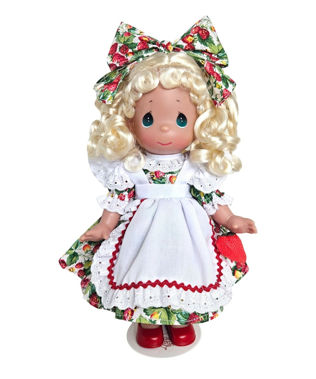 The Doll Maker's You're Berry Sweet doll, a 12" vinyl doll with blonde curly hair, wearing a strawberry print dress and white apron.
