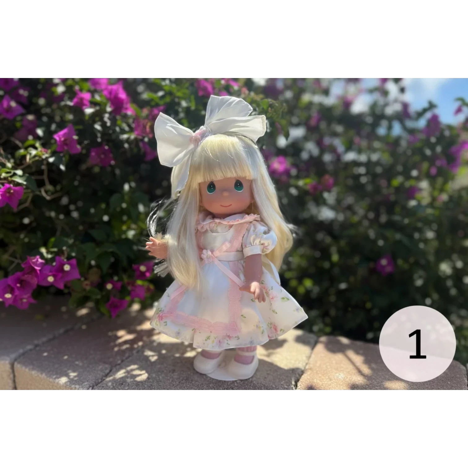 The Doll Maker's Spring Bouquets 12-inch doll with blonde hair, blue eyes, wearing a white floral dress with pink trim and a large white bow.