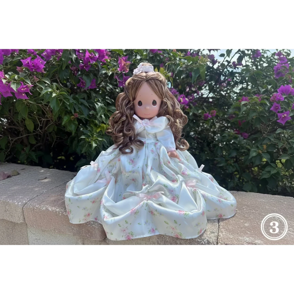 The Doll Maker Spring Bouquets 12 inch doll with long brown curly hair wearing a white floral print dress with pink bows.