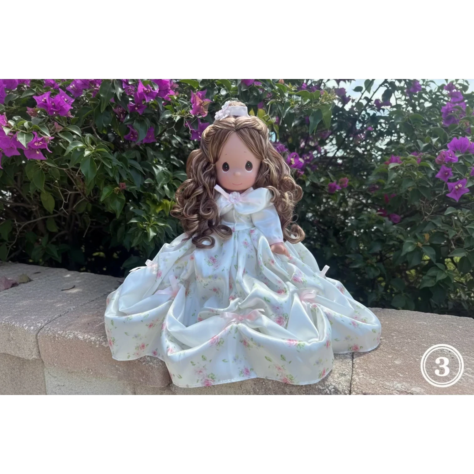 The Doll Maker Spring Bouquets 12 inch doll with long brown curly hair wearing a white floral print dress with pink bows.