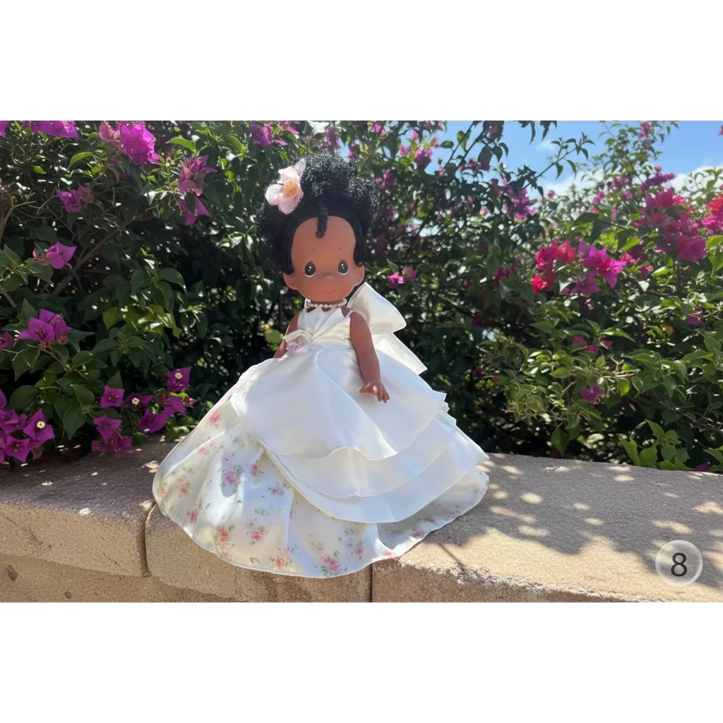 The Doll Maker's 12-inch Spring Bouquets doll with black hair, wearing a white satin gown with floral print underskirt and a pink flower accessory.