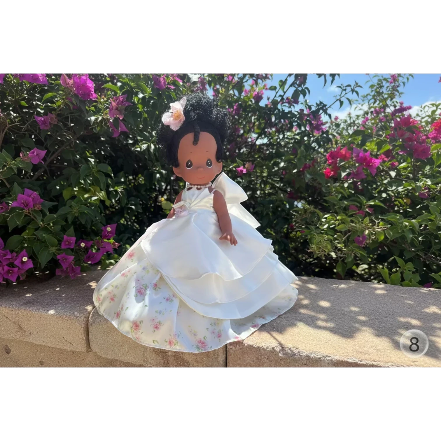 The Doll Maker's 12-inch Spring Bouquets doll with black hair, wearing a white satin gown with floral print underskirt and a pink flower accessory.