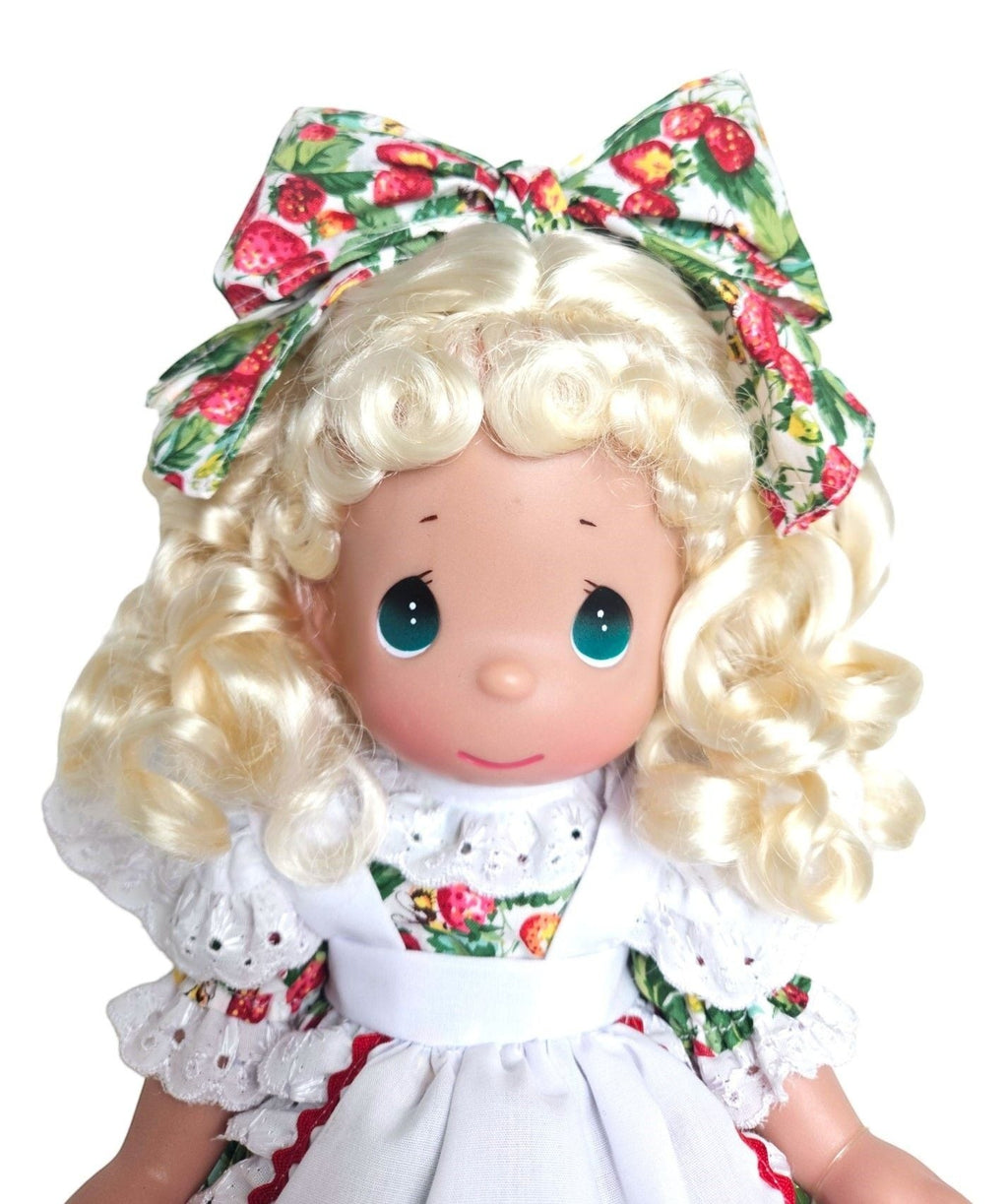 The Doll Maker blonde doll wearing a strawberry print dress and bow. Vinyl and fabric construction.